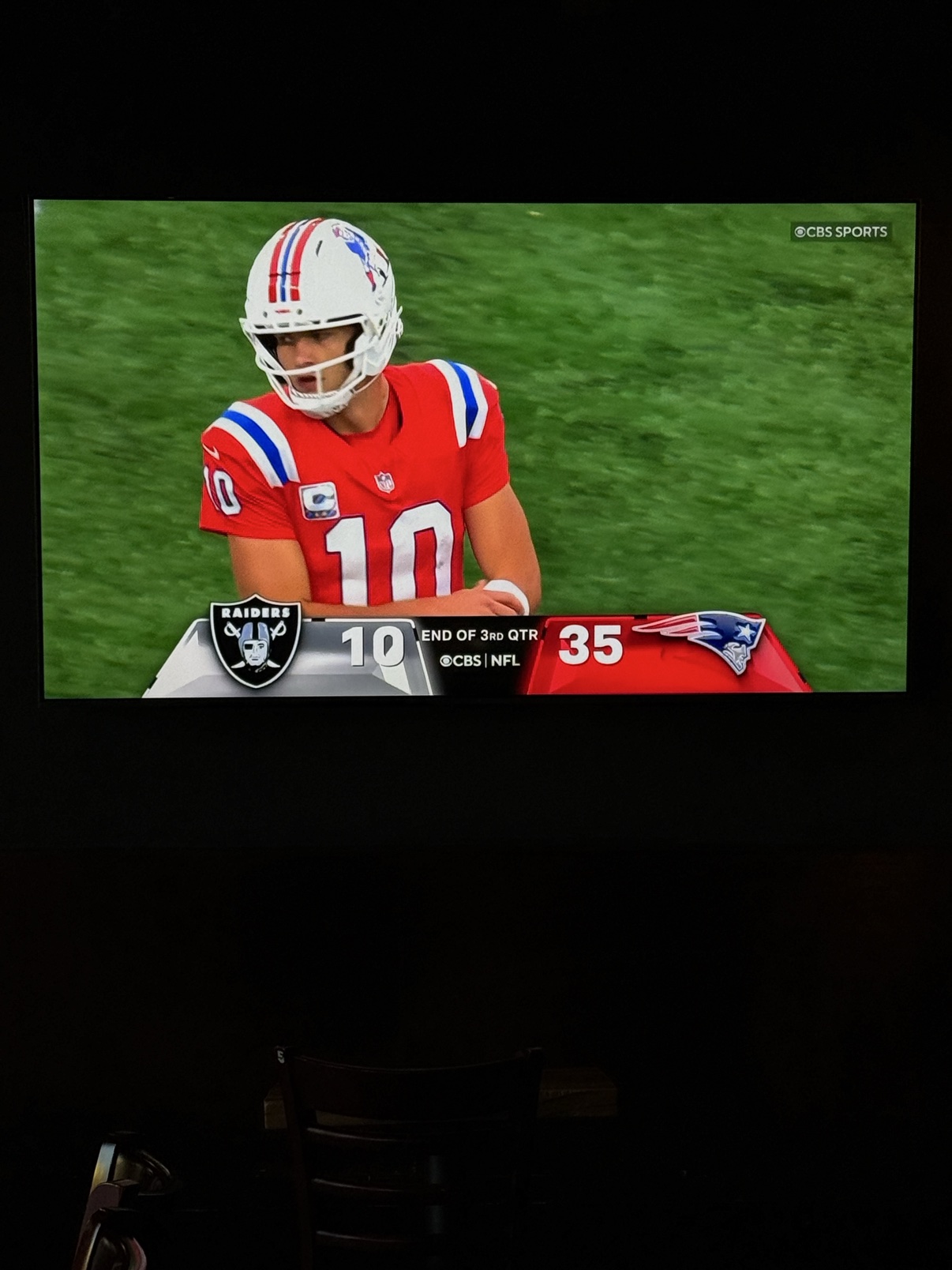 Drake Maye on the TV in his red Patriots jersey, the score bug reading Raiders 10, Patriots 35 at the end of the third quarter